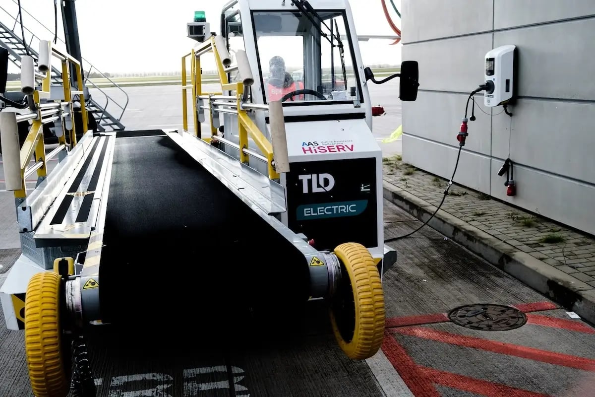 Elektrisches Fahrzeug mit Gepäckrampe für das Be- und Entladen von Koffern am Flughafen BER Berlin Brandenburg wird an der Luftgastbrücke an einer Virta Ladestation geladen