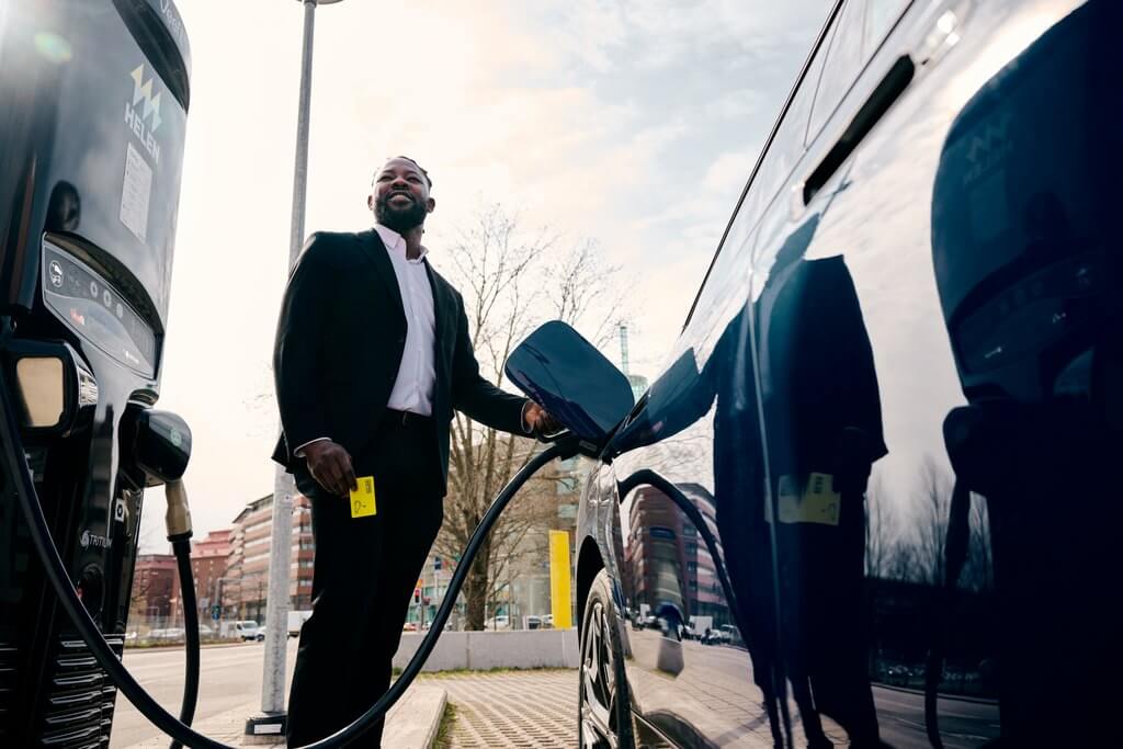 Ett foto på en man som står mellan en elbil och en laddstation och laddar elbilen