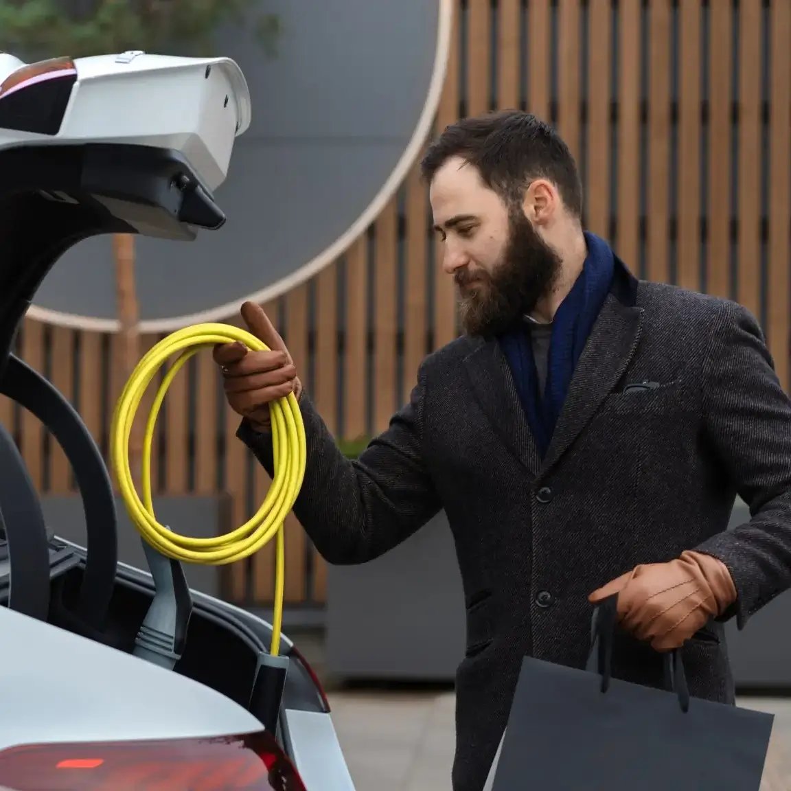 Professioneller Geschäftsmann legt Ladekabel in den Kofferraum eines Elektrofahrzeugs