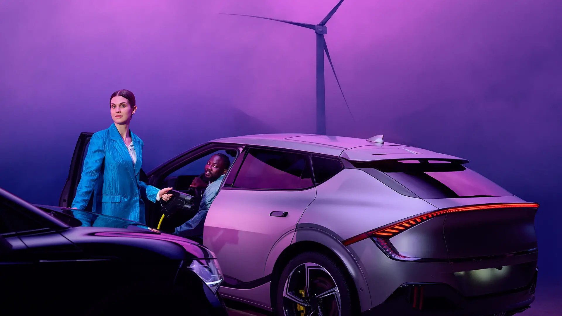 Couple en train de charger un véhicule électrique sur fond violet d'éolienne