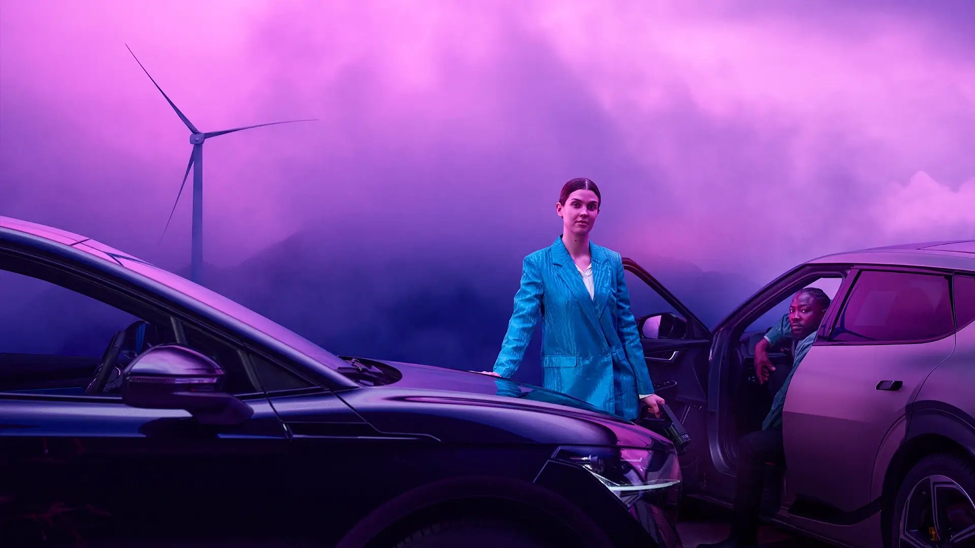 Seisova nainen, istuva mies sähköautoja, tuulivoimala, purppura taivas