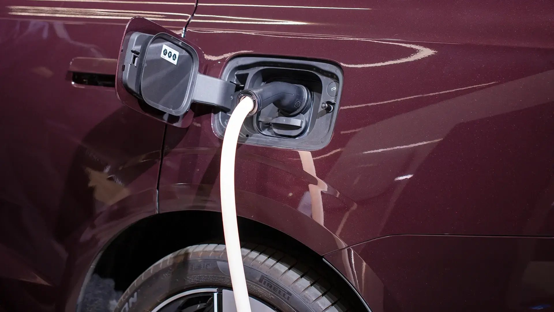 Close-up of a burgundy electric vehicle charging via AC connector at rear-left side panel