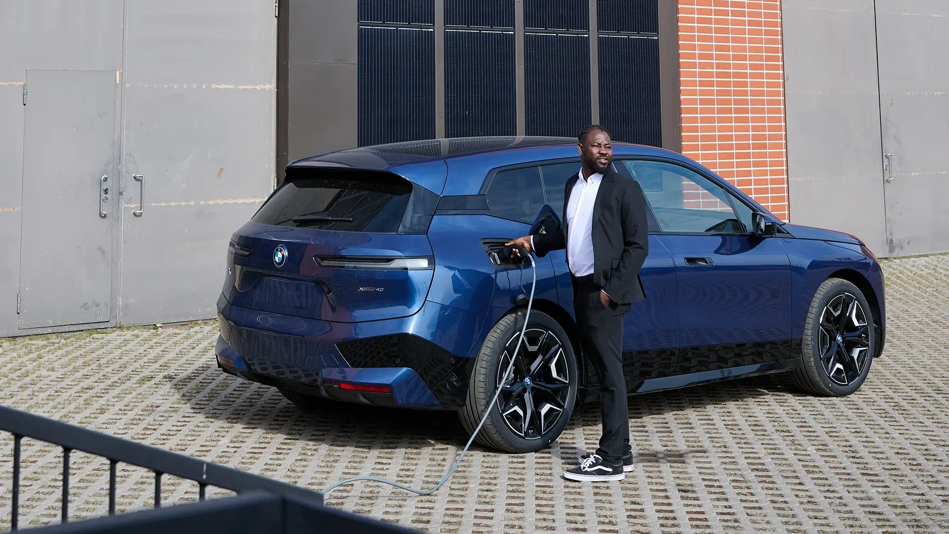 Mann hält Ladekabel in der Hand und lädt blaues SUV E-Auto im urbanen Gebiet