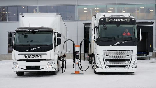 zwei elektrische Lkw oder E-Trucks laden an einer Schnellladestation in einem Logistikzentrum