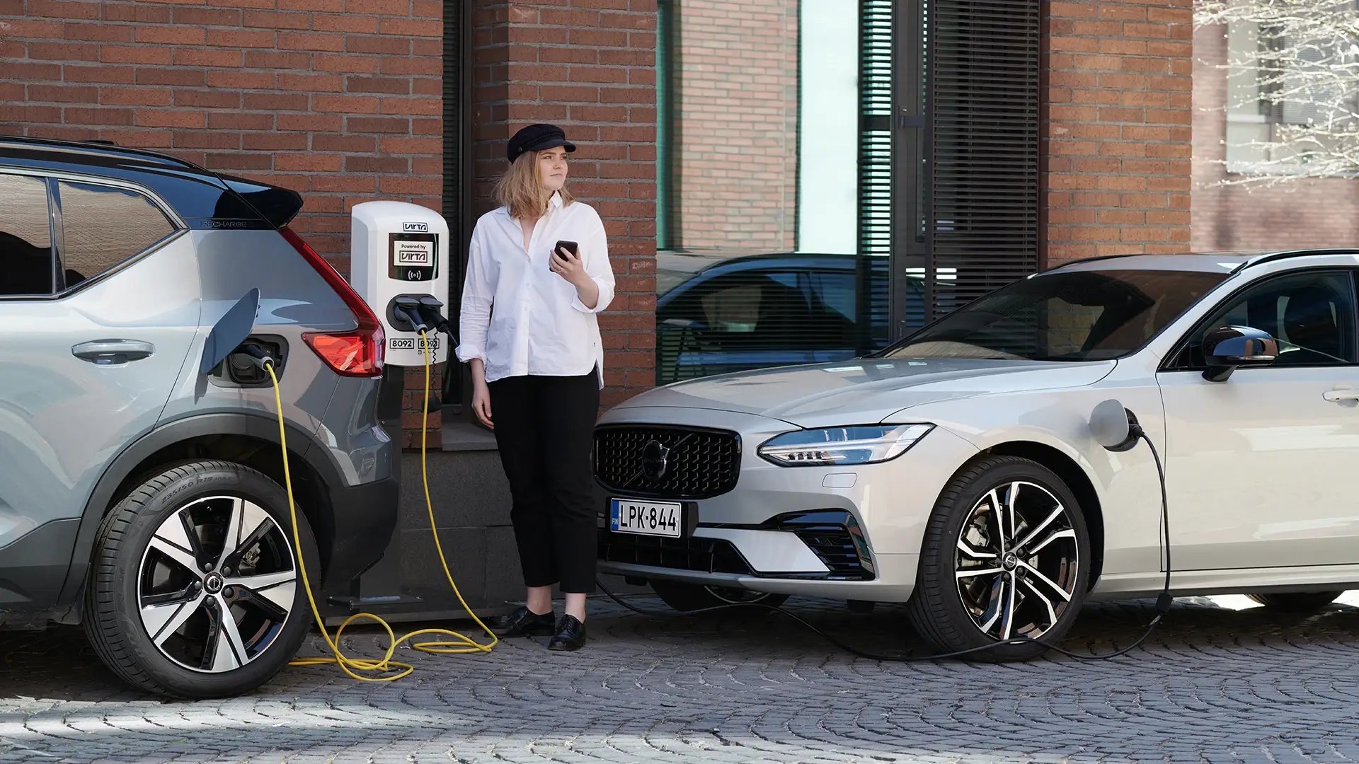 Woman with smartphone urban EV AC charging point sidewalk