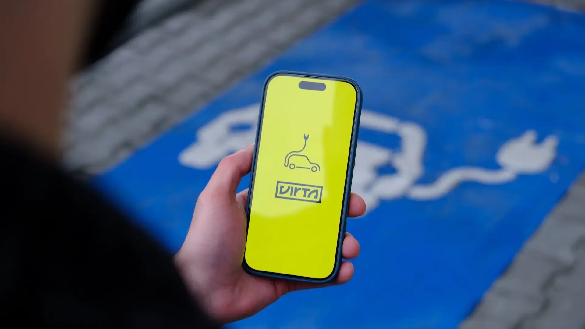 Men holding smartphone with Virta app in front of parking lot for charging