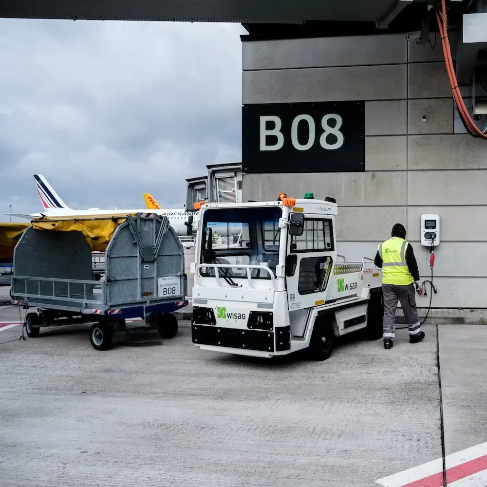 BER Flughafen Berlin Brandenburg Mitarbeiter lädt elektrisches Zugfahrzeug an einer Virta Ladestation auf dem Vorfeld des Flughafens auf
