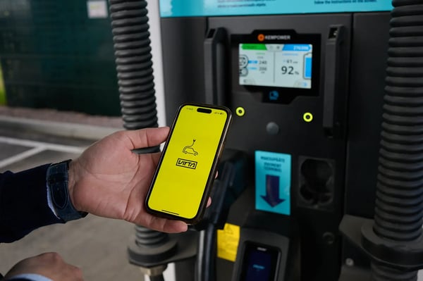 A hand holding a mobile phone with Virta app in front of a Faast's HPC Kempower charger