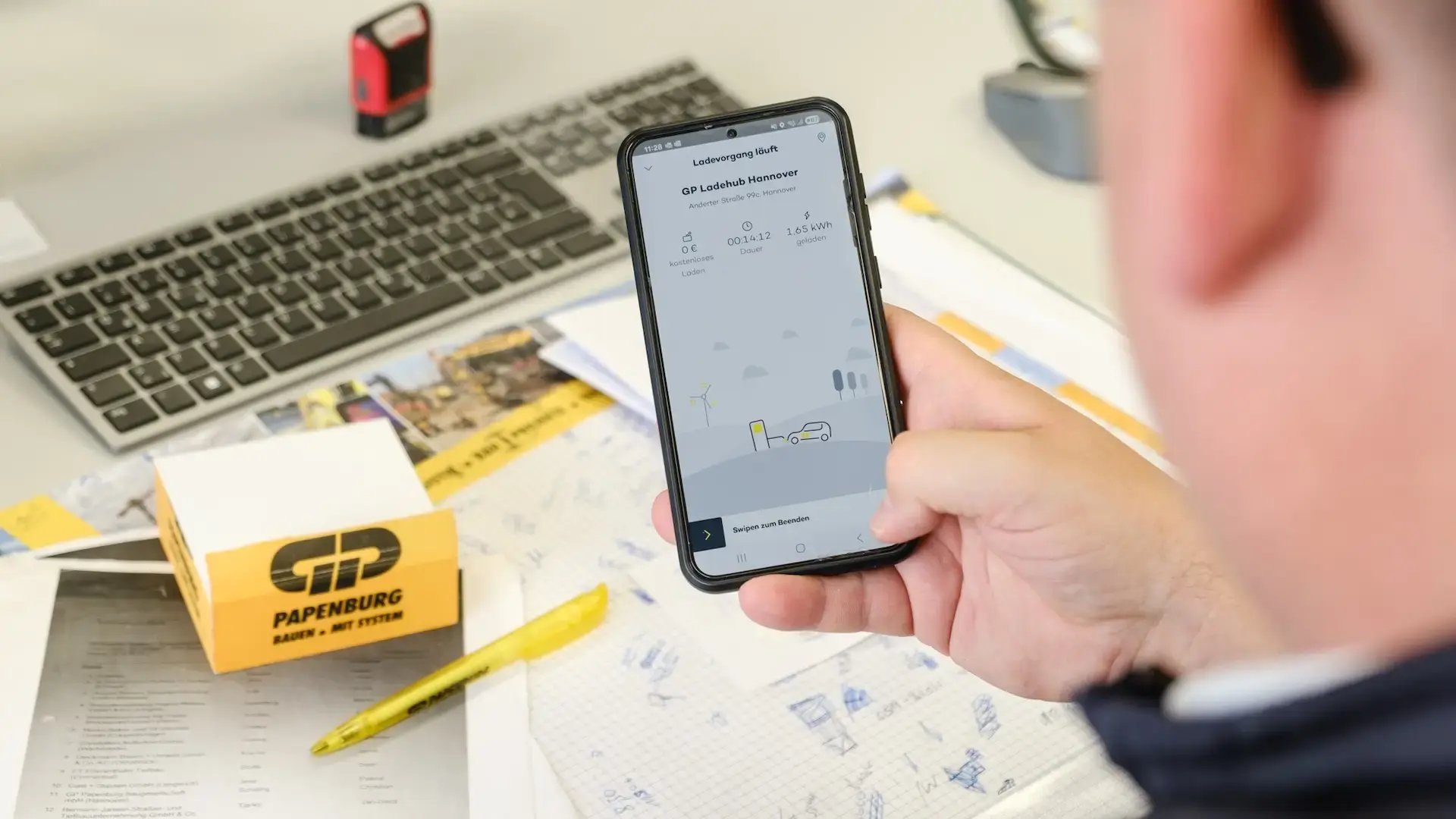 Man holding smartphone at desk checking charging status on Virta app in GP Papenburg AG office