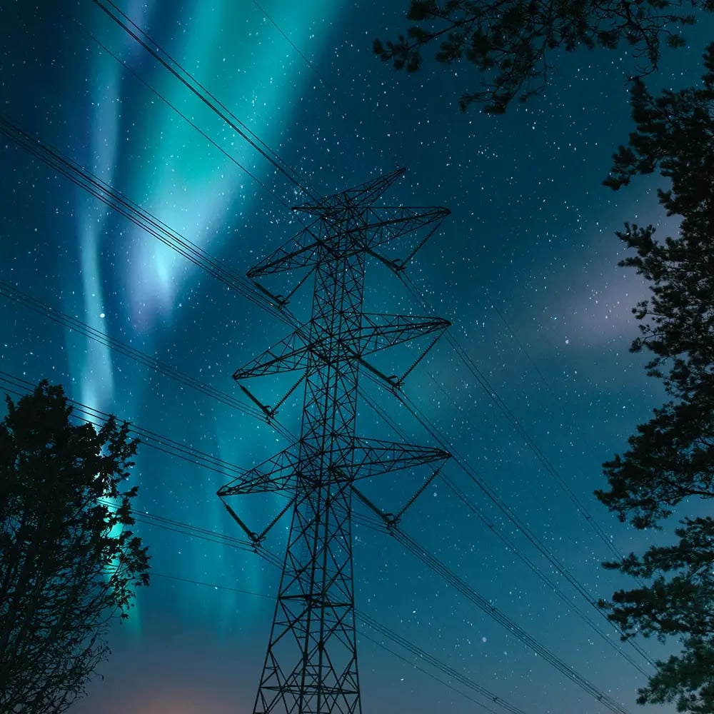 Norrsken synligt bakom kraftledningar och träd mot en natthimmel
