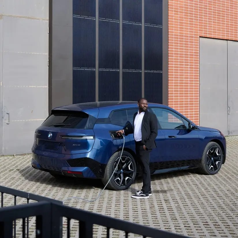 Mann hält Ladekabel ind er Hand und lädt blaues SUV E-Auto in einer urbanen Umgebung