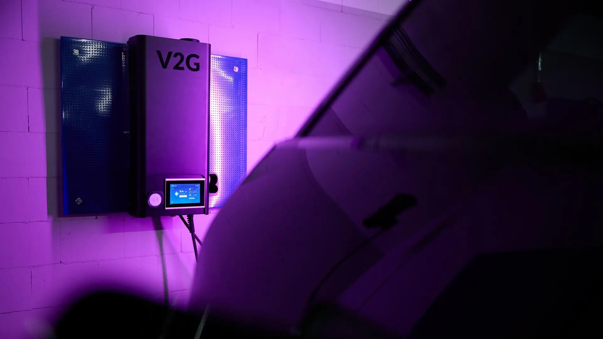 Vehicle-to-Grid V2G Ladestation angeschlossen an E-Auto in pinkem Neonlicht in Garage