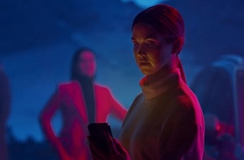 Foto på två kvinnor, varav den i förgrunden håller i en mobiltelefon och tittar på den