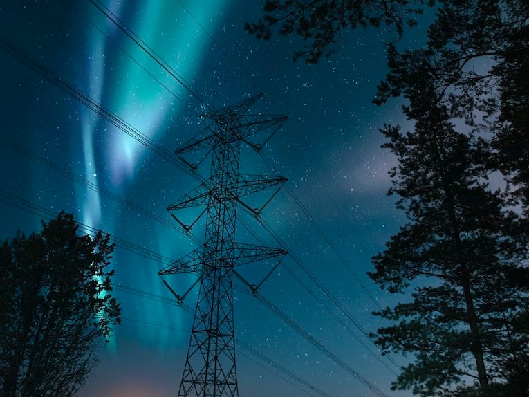 Foto på en elledning i en skog i skymningen med norrsken på himlen