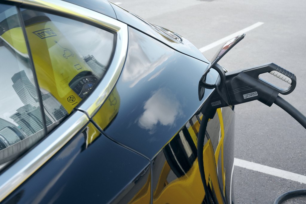 Bild på elbil som laddas med siluetten av en elbilsladdare och en stad som reflekteras i bilens lack