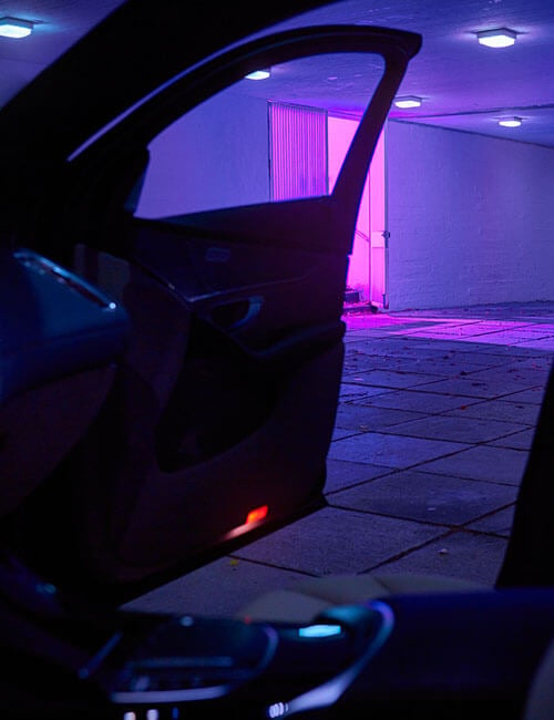 Bild tagen inifrån en elbil med en dörr öppen ut mot ett parkeringsgarage i lila ljussken 