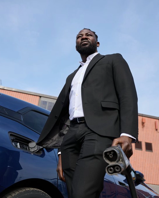 Foto på mat ståendes bredvid en elbil, hållande en CCS-laddkabel i ena handen