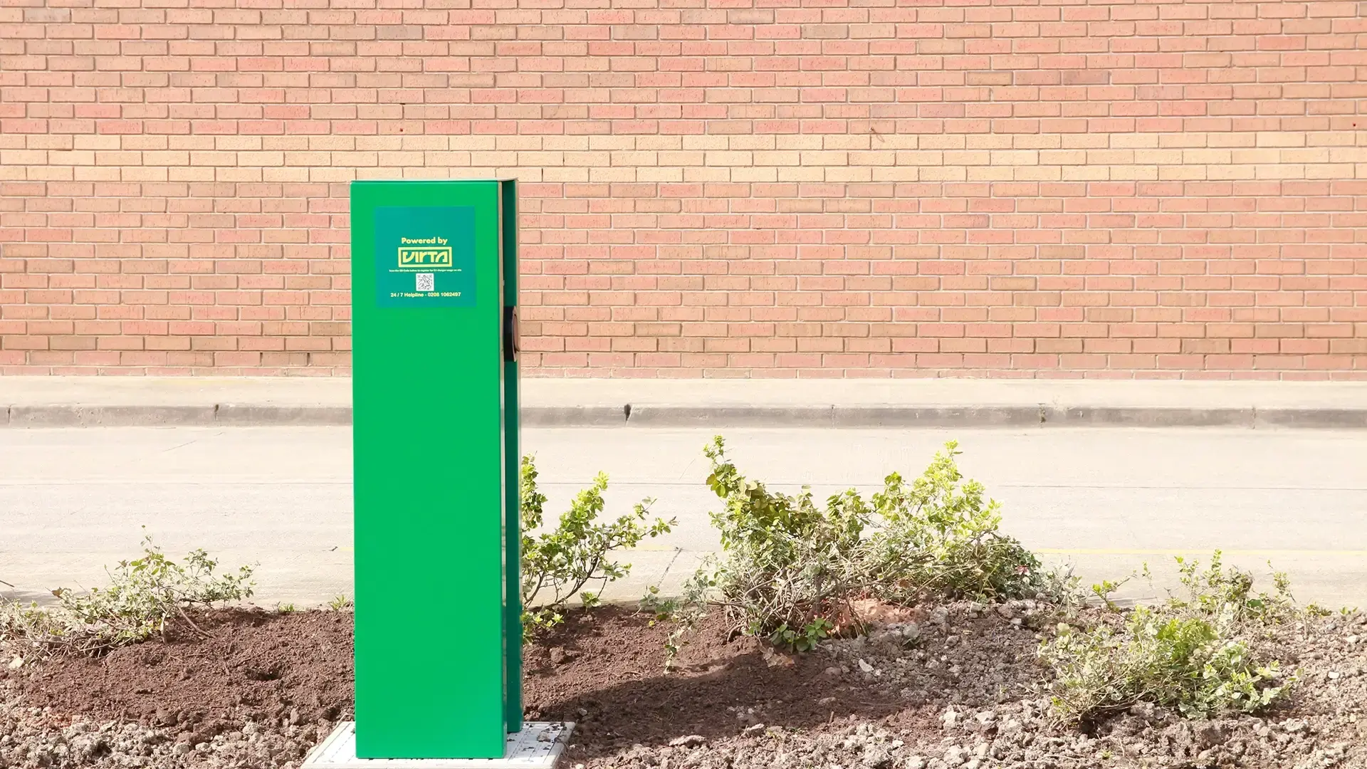 Green EV charger in front of a brick wall