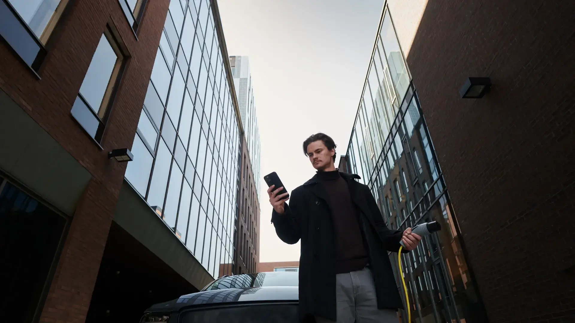Mann hält smartphone in der Hand und Ladekabel für Ladestation in der anderen im urbanen Gebiet