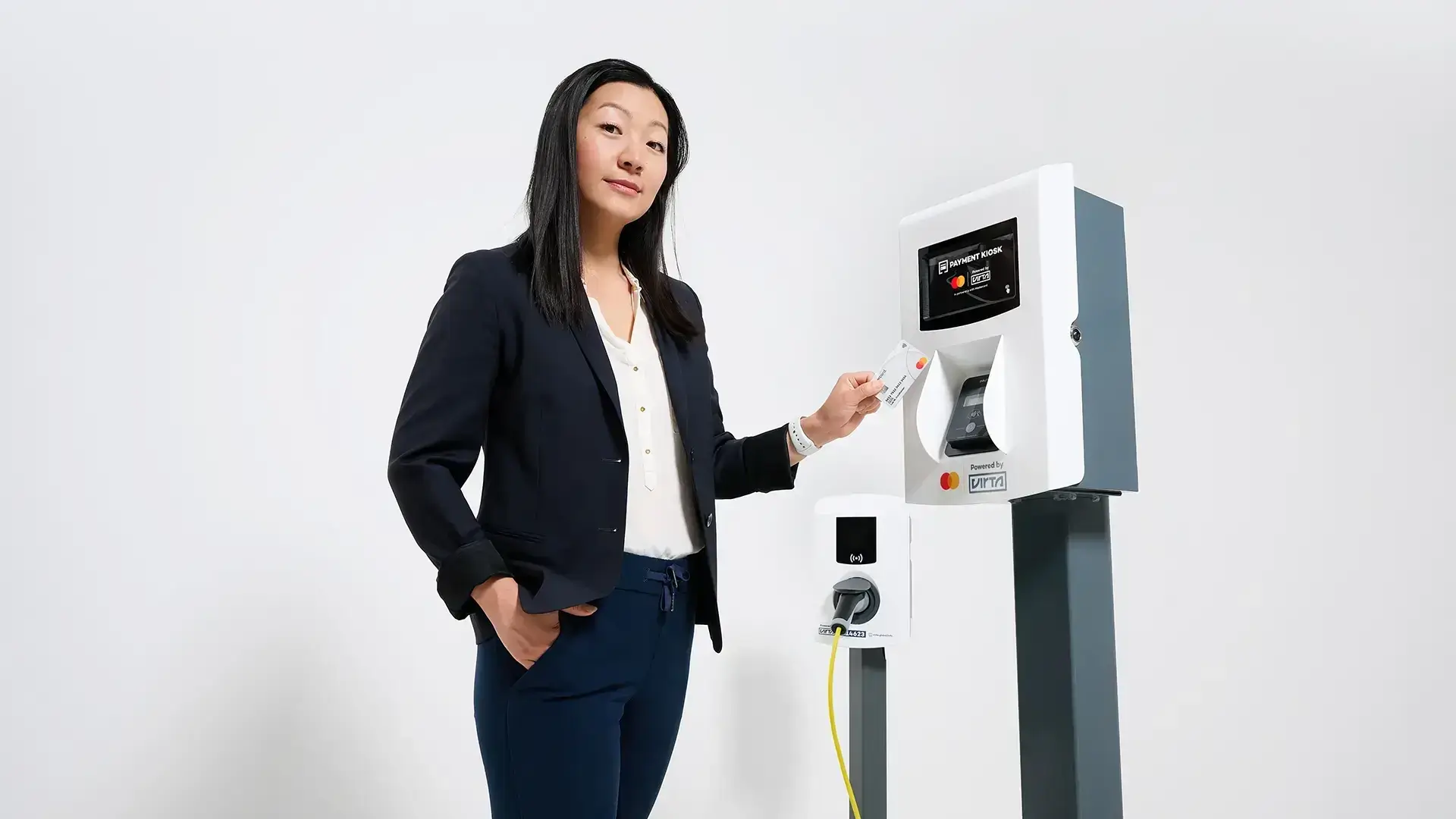 Woman standing beside a Virta payment kiosk and an AC charging station