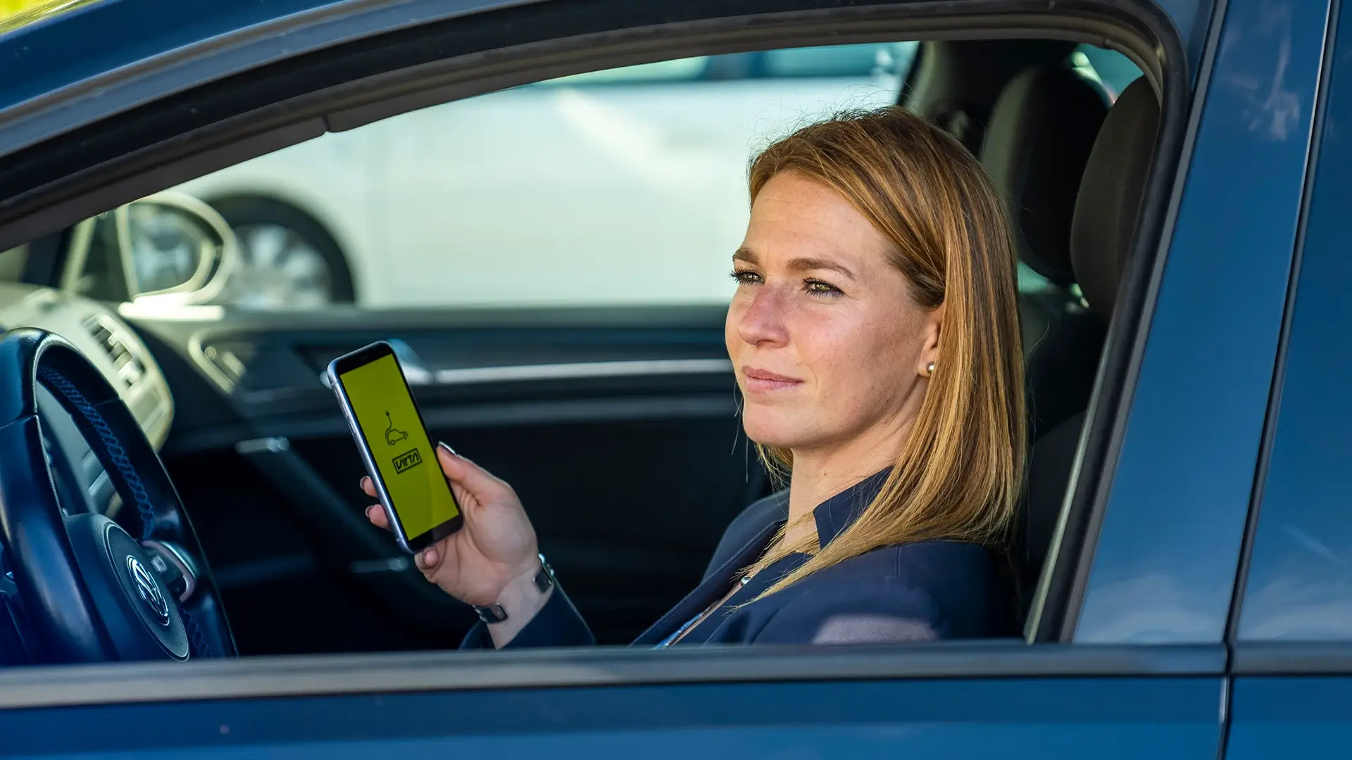 Aurélie Allier, Direktorin am FREY Standort Clos du Chêne sitzt im E-Auto mit Virta App auf Smartphone