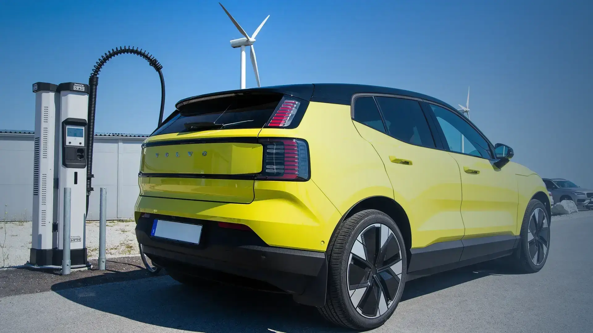 Yellow EV charging at Kempower Satellite charging station with wind turbines renewable energy production in the background